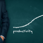 Business professional standing beside an upward productivity growth chart on a chalkboard.