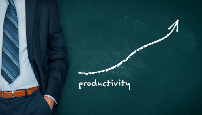 Business professional standing beside an upward productivity growth chart on a chalkboard.